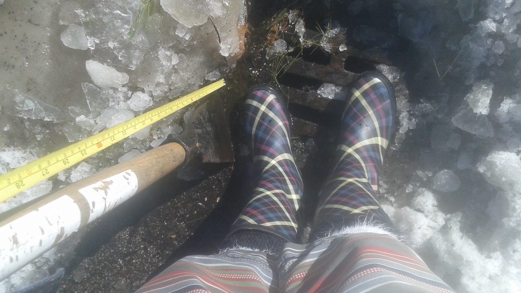 my feet in rain boots, standing next to my ice chipper on the storm drain I just cleared